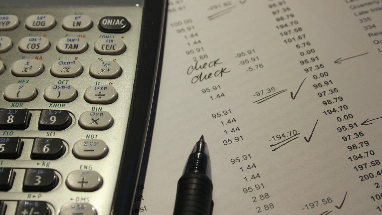 Mains calculant un budget de courses avec une calculatrice, un ticket de caisse et un carnet