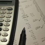 Mains calculant un budget de courses avec une calculatrice, un ticket de caisse et un carnet